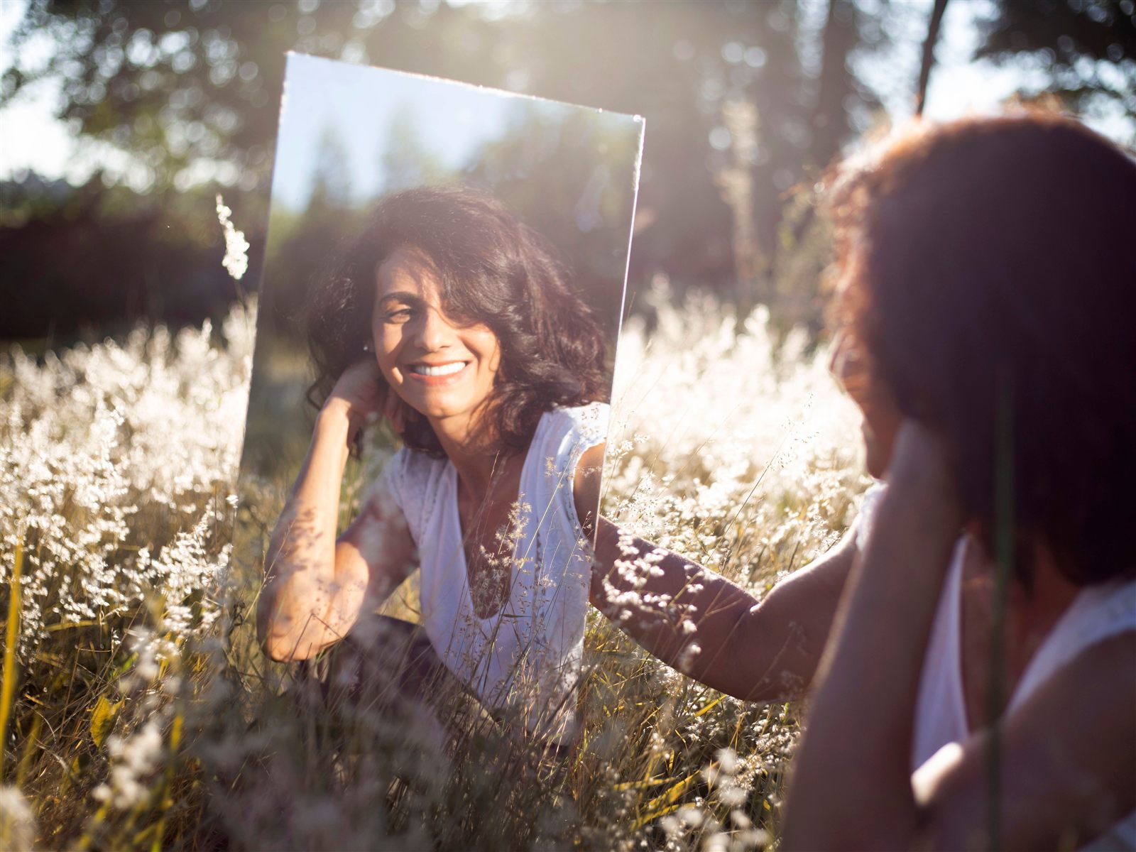 Mujer mirándose con una sonrisa en un espejo en mitad del campo